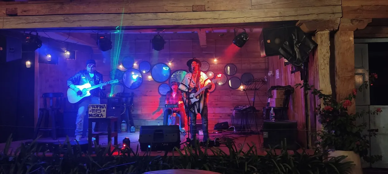 Mateo Acevedo canta en una presentación acústica con luces de colores en un bar rústico.