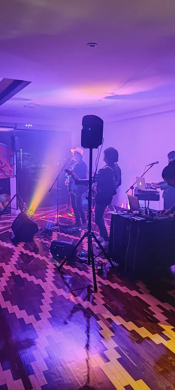 La banda de Mateo Acevedo toca en vivo bajo intensas luces moradas en un salón de eventos.