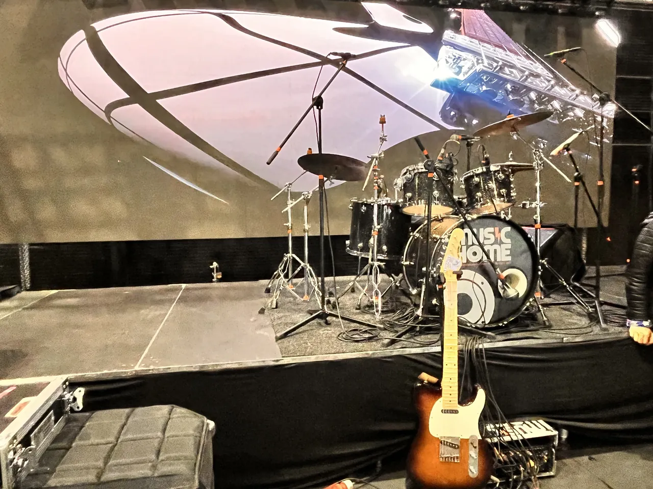 Montaje de batería y guitarra eléctrica sobre el escenario con pantalla curva antes de una presentación en vivo.