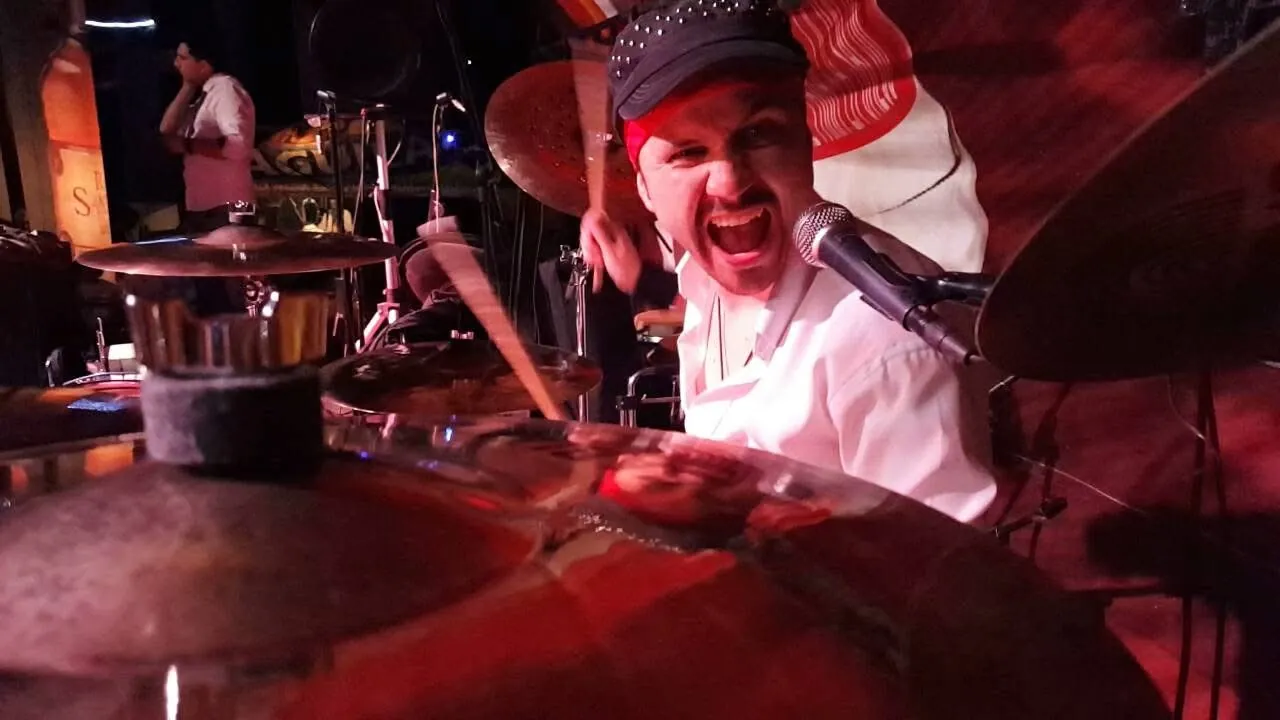 El baterista de la banda de Mateo Acevedo toca con intensidad bajo luces rojas durante un show en vivo.