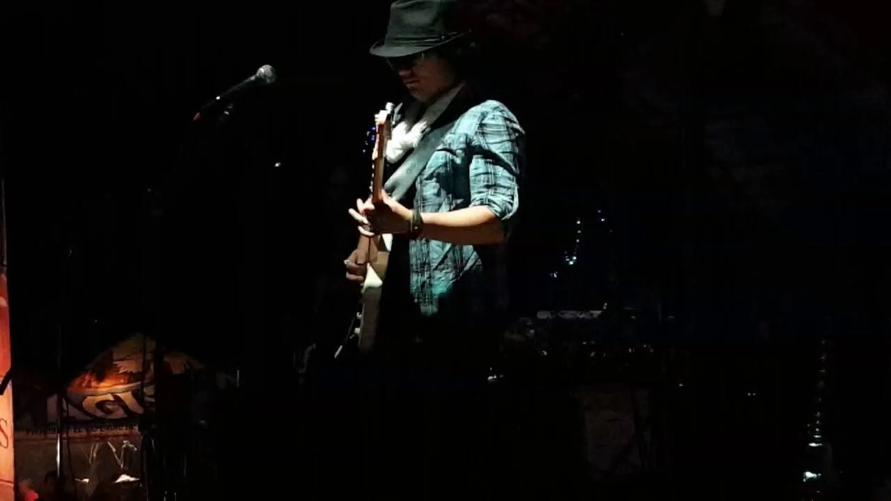 Mateo Acevedo con sombrero toca la guitarra y canta al micrófono en una presentación íntima de bar.