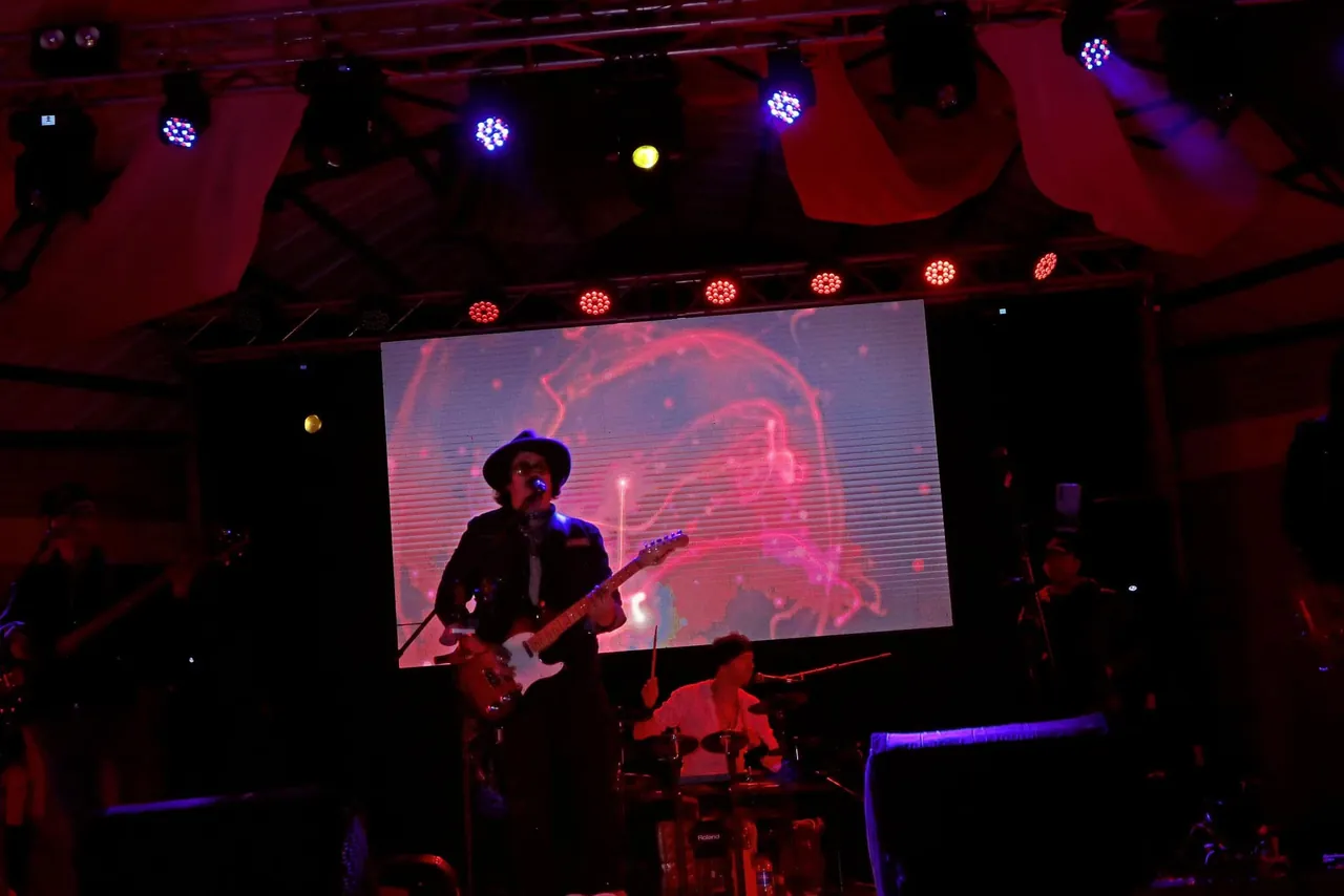 Mateo Acevedo canta y toca guitarra eléctrica frente a una pantalla LED en un concierto.