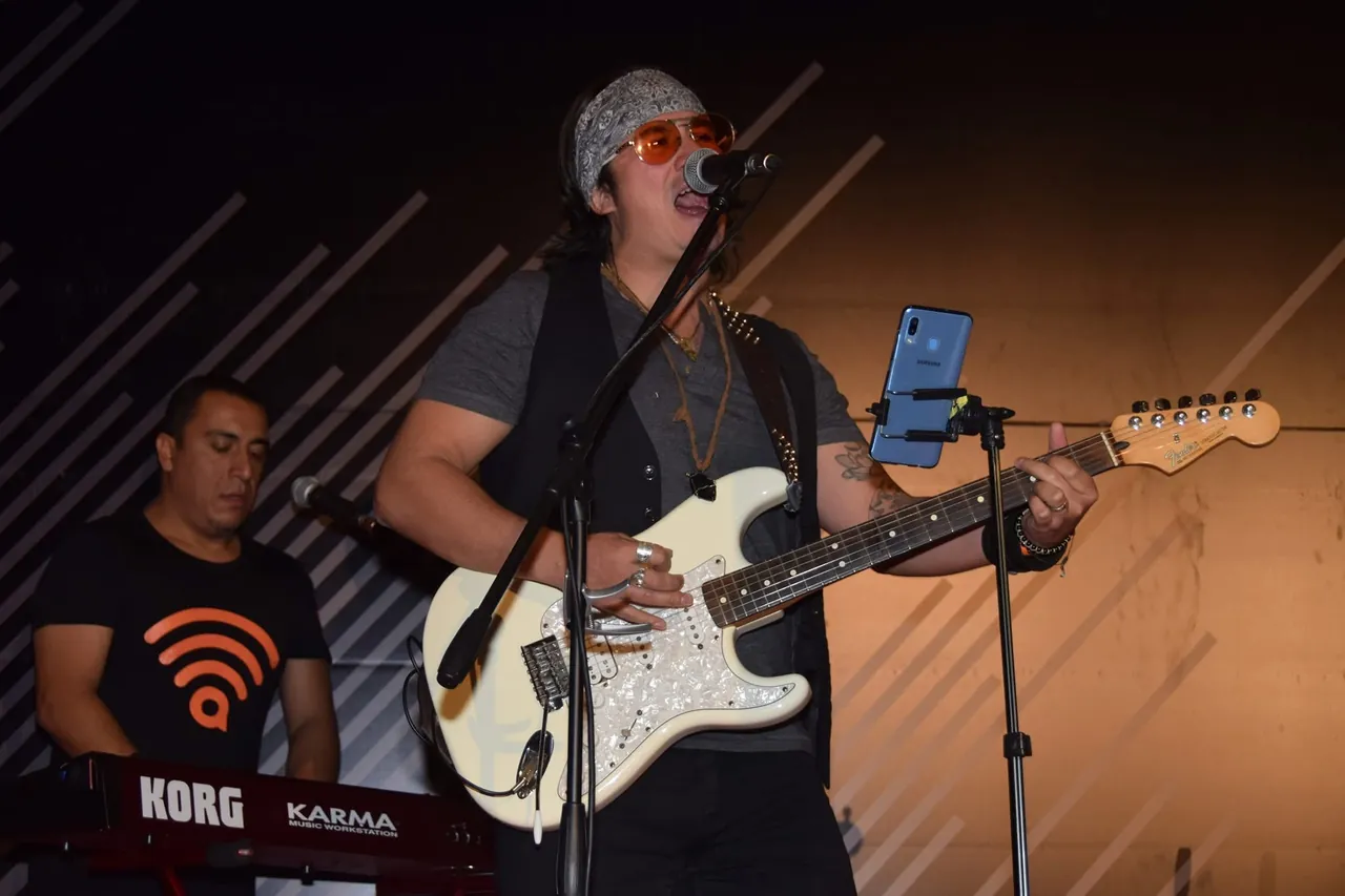 Mateo Acevedo cantando y tocando guitarra eléctrica en vivo junto a su tecladista durante un evento.
