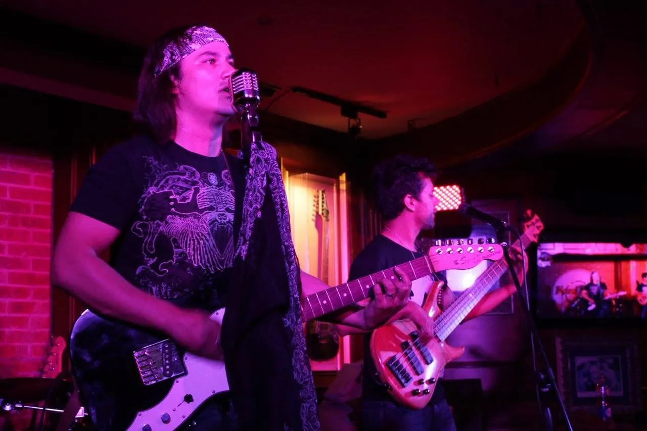 Mateo Acevedo canta al micrófono vintage mientras toca la guitarra con su bajista en un show en vivo.
