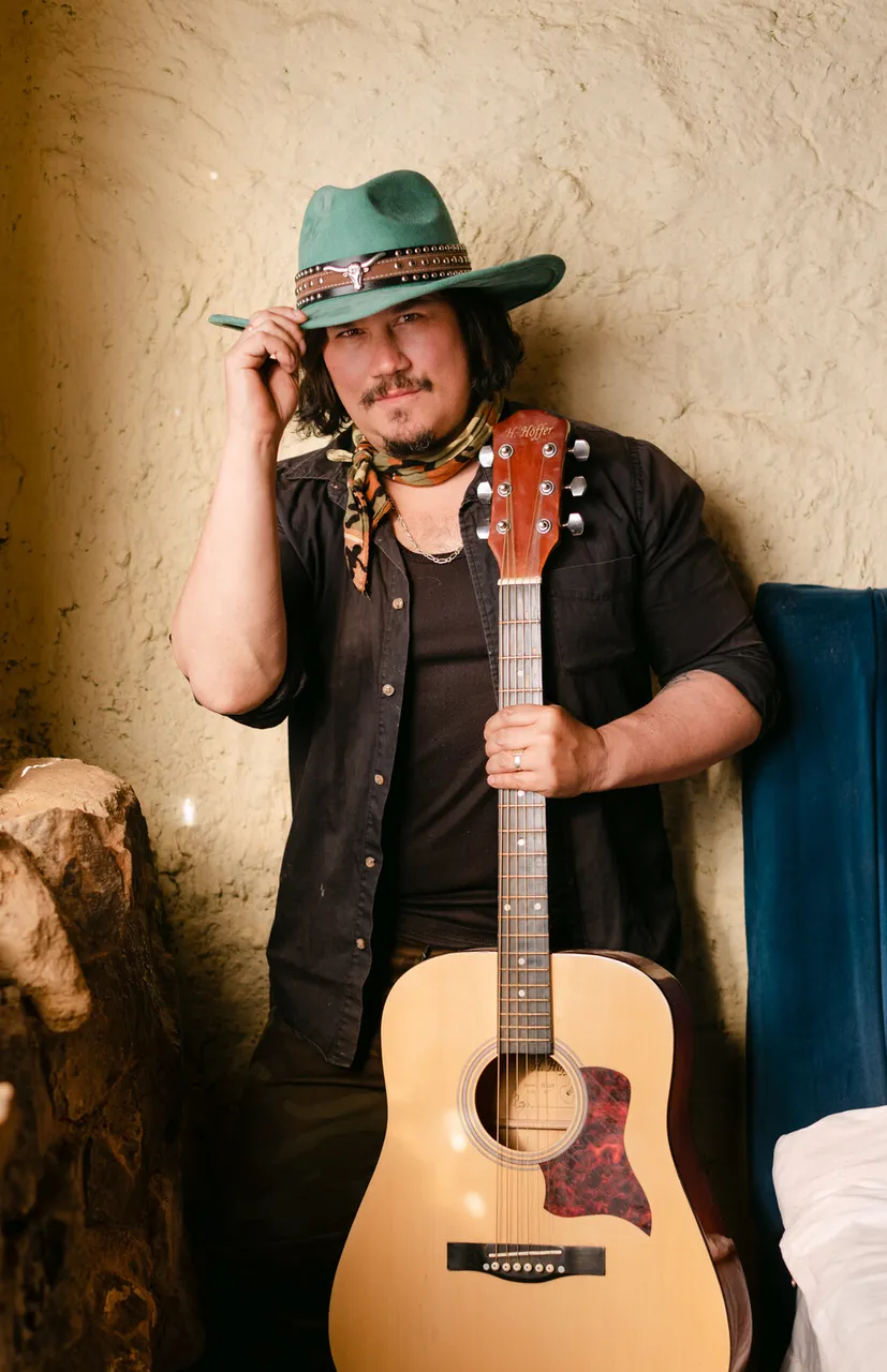 Mateo Acevedo de pie con sombrero y guitarra acústica