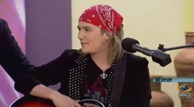 Mateo Acevedo durante una entrevista en televisión, sentado con su guitarra y pañoleta roja en el set.