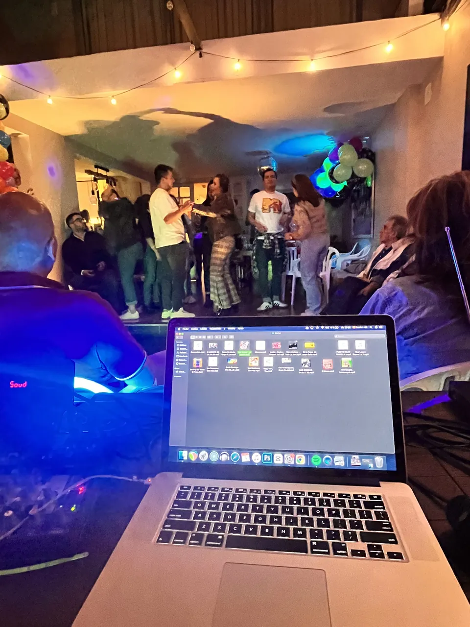 Montaje de música en vivo con laptop sobre la consola durante un evento social con globos e invitados.