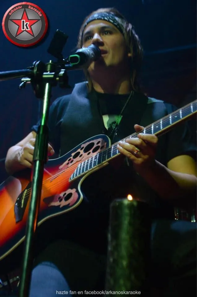 Mateo Acevedo cantando mientras toca su guitarra acústica durante un show en vivo con luz tenue.