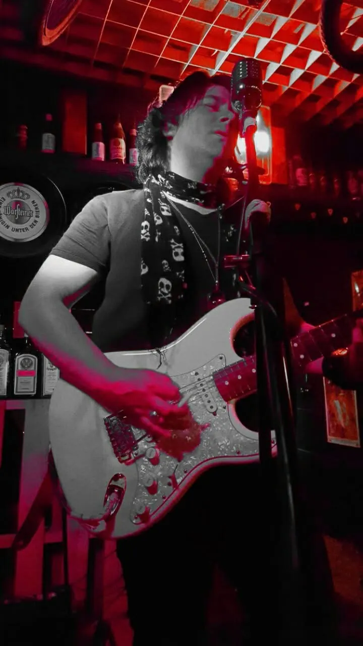 Mateo Acevedo toca la guitarra eléctrica frente a un micrófono vintage en una presentación de rock en un bar.