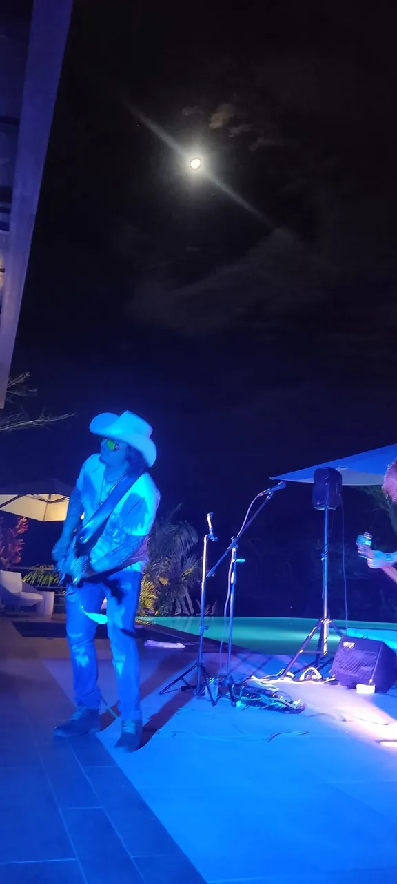 Mateo Acevedo toca la guitarra bajo la luna llena en un concierto nocturno al aire libre con luz azul.