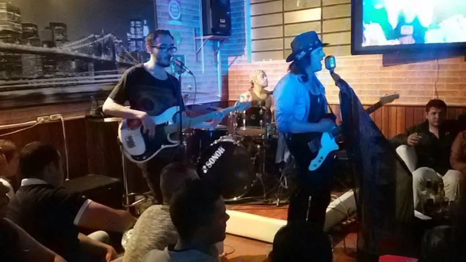 Mateo Acevedo canta con sombrero mientras su banda toca para un público cercano en un bar lounge.