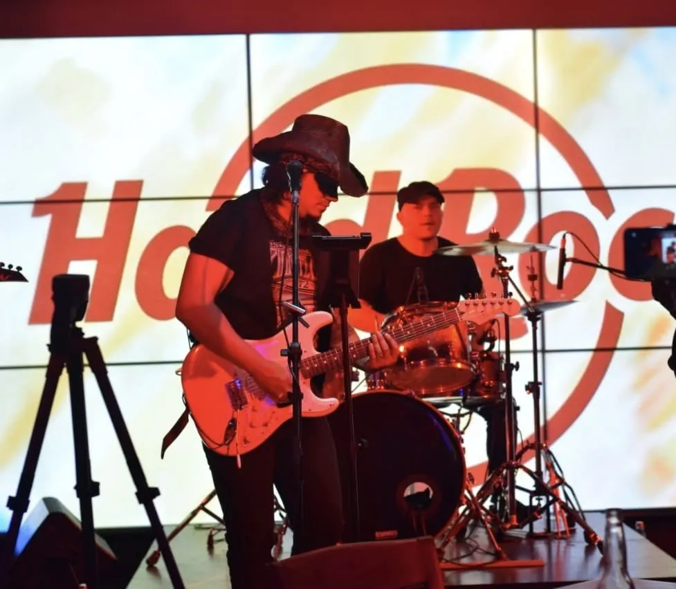 Mateo Acevedo tocando guitarra eléctrica en un show de rock en vivo frente a una gran pantalla con logo de rock.